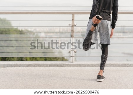 Young fit slim sportsman male athlete stretching his legs before jogging running on city bridge in urban area in sporty fitness clothes and trainers. Warming-up exercises outdoors. Royalty-Free Stock Photo #2026500476