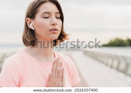 Young Caucasian woman female athlete meditating before doing yoga exercises, praying to the God, listening to the podcast, favorite relaxing music, soundtrack. Concentration and serenity concept.