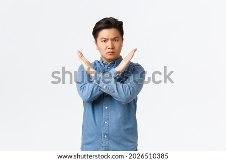 Serious-looking concerned asian male student showing forbid gesture, making cross sign to stop someone, disagree and prohibit action, telling no, enough, being fed up, standing white background Royalty-Free Stock Photo #2026510385