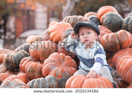 Blonde baby boy sitting on a pile of ripe pumpkins.