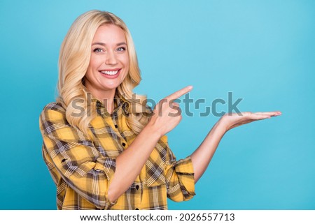 Portrait of lovely cheerful wavy-haired woman holding on palm demonstrating copy space isolated over bright blue color background