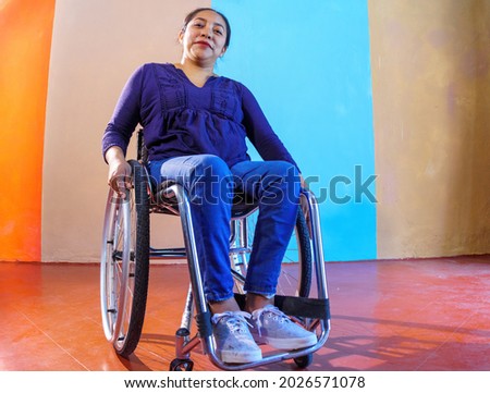 Middle-aged Hispanic woman with disabilities on a wheelchair against a colorful background Royalty-Free Stock Photo #2026571078