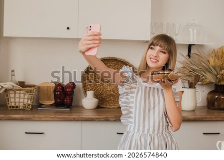 A beautiful girl pastry chef or housewife makes a selfie on the phone. Culinary blog concept.