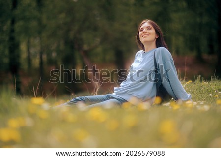 
Happy Young Woman Sitting in the Grass Enjoining Nature. Carefree person resting in a countryside field experiencing mindfulness and calmness 
 Royalty-Free Stock Photo #2026579088