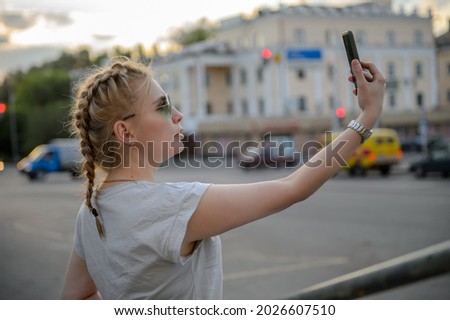 The girl takes pictures of herself on the phone on the streets of the city.