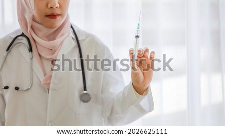 Close up portrait of young female muslim asian doctor holding up medical syringe for giving injection of vaccine.