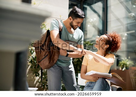 Young happy students greeting with fist while meeting at the university.  Royalty-Free Stock Photo #2026659959