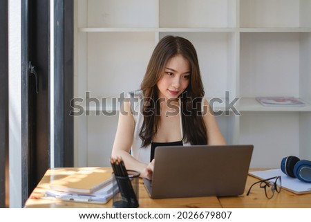 Asian Business woman sitting in office with laptop computer on wooden desk.