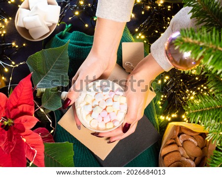 Woman hands holding mug of hot chocolate with marshmallows winter festive background with ornaments 