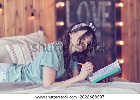 lifestyle soft image of pretty young woman sitting on her cozy bed and making notes to her diary. Fall season mood.