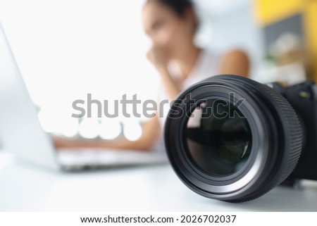 Camera lens on background of woman working at computer