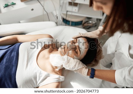 High angle view of aesthetician performing beauty procedure on woman face, removing the rest of cosmetic product using special wet serviettes. Professional skin care in cosmetology clinic Royalty-Free Stock Photo #2026704773