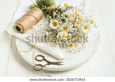 Bouquet of beautiful chamomile flowers, scissors and rope on light wooden background