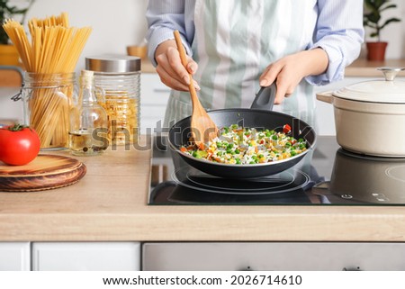 Woman cooking tasty rice with vegetables on stove in kitchen, closeup Royalty-Free Stock Photo #2026714610