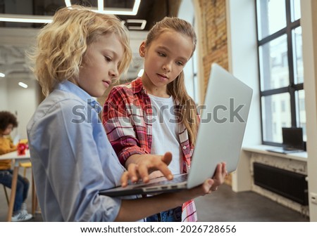 Two curious kids, little boy and girl using laptop while standing in a classroom during STEM lesson Royalty-Free Stock Photo #2026728656