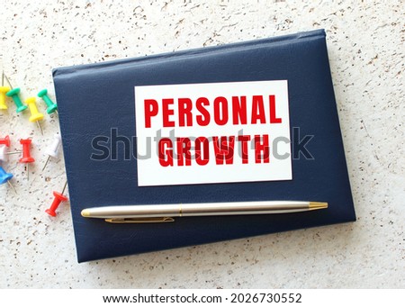 Text PERSONAL GROWTH on a business card lying on a blue notebook next to the pen. Business concept.