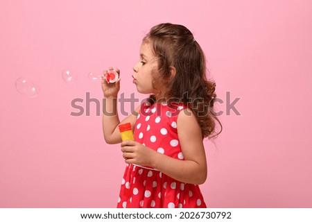 Side portrait of a cheerful beautiful baby girl blowing soap bubbles, isolated over pink background with space for text . Gorgeous child playing with soap bubbles. Summer children leisures concept Royalty-Free Stock Photo #2026730792