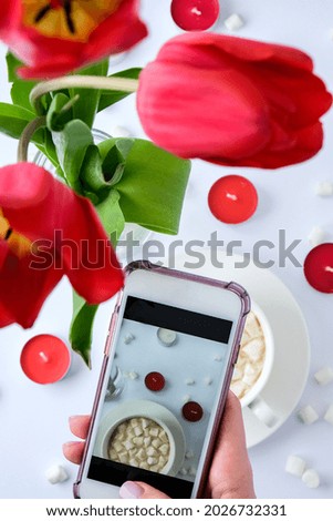 Red tulips candles White cup of cacao marshmallows morning breakfast. Female hand taking photo. Blogger. Valentines Womans Mothers day