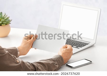 Man with blank paper sheet at table in office