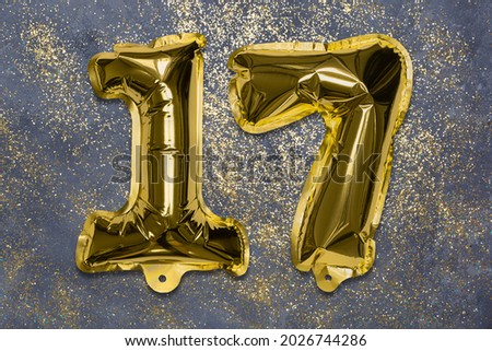 The number of the balloon made of golden foil, the number seventeen on a gray background with sequins. Birthday greeting card with inscription 17. Numerical digit, Celebration event, template.