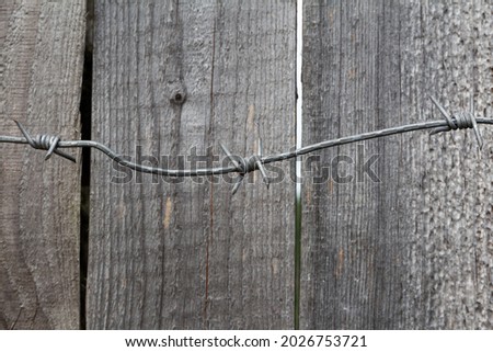 Barbed wire on rough gray planks of an old wooden fence
