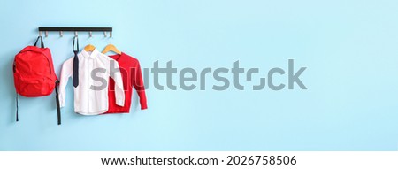 Modern school uniform and backpack hanging on color wall Royalty-Free Stock Photo #2026758506