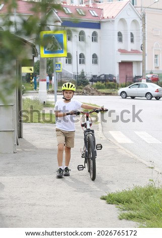 boy cyclist in a safety helmet walks along the road and holds a bike