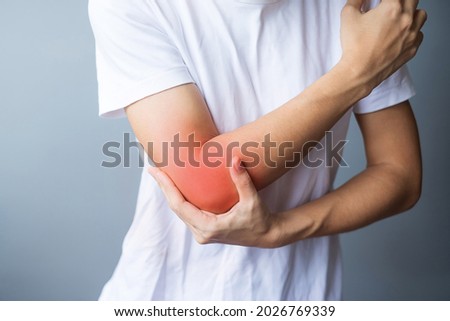 Young adult female with her muscle pain on gray background. Woman having elbow ache due to lateral epicondylitis or tennis elbow. injuries and medical concept Royalty-Free Stock Photo #2026769339