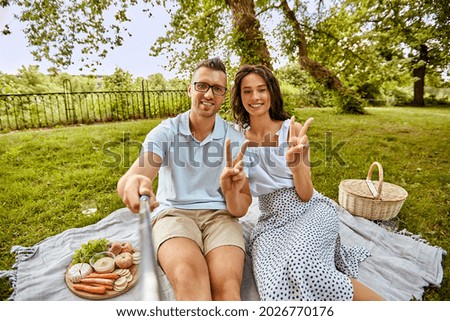 leisure and people concept - happy couple taking picture with selfie stick and showing peace sign on picnic at summer park