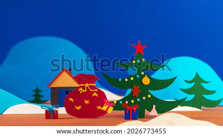 Santa's bag with gift boxes falls under a Christmas tree with a garland and decorations on a background of snow-capped mountains