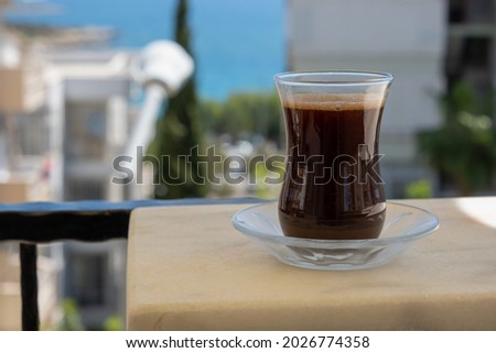 Turkish coffee in transparent traditional glass against buildings and sea view with trees in summer.