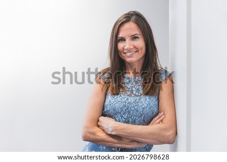 Smiling businesswoman in the office. Young woman standing with folded arms, front view, white background