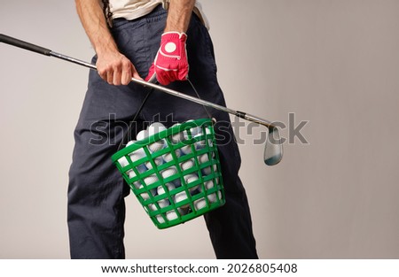 Golfer wearing glove and holding an iron and a basket full of golf balls to go to the driving range