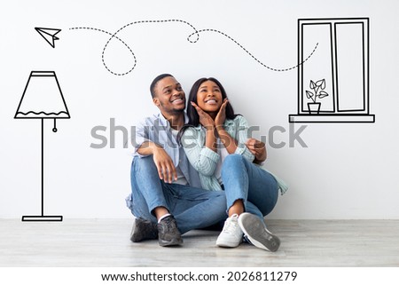 Loving african american couple imagining interior of their new apartment, embracing and sitting on floor near wall with doodle drawings, planning relocation. Creative collage Royalty-Free Stock Photo #2026811279