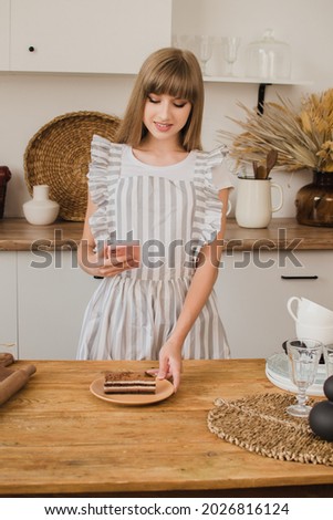 Beautiful girl pastry chef or housewife makes a photo of dessert on the phone. The concept of a culinary blog or pastry courses.