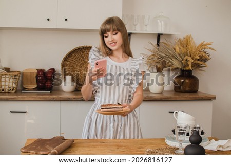 Beautiful girl pastry chef or housewife makes a photo of dessert on the phone. The concept of a culinary blog or pastry courses.