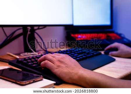 Professional gamer's hands on a backlit keyboard are playing E-Sport games online on computer in dark room with neon light.