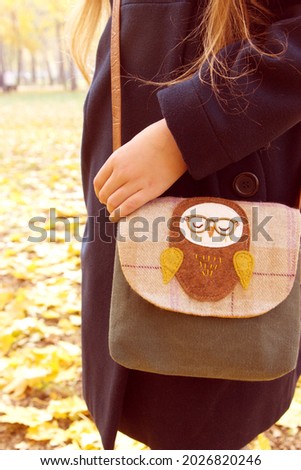 Little girl walks in park with owl handbag.