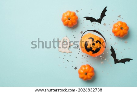 Top view photo of halloween decorations pumpkin basket silver sequins stars bat and ghost silhouettes on isolated pastel blue background with copyspace