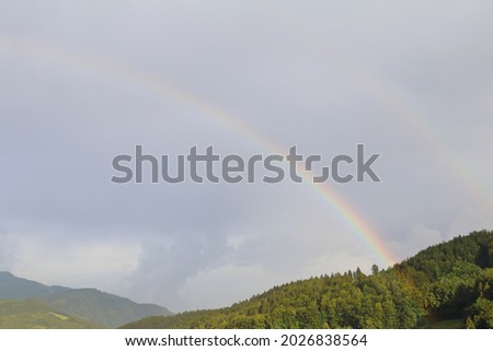 Rainbow after rain on a blue sky background with some clouds. On the bottom of the picture are some hills.