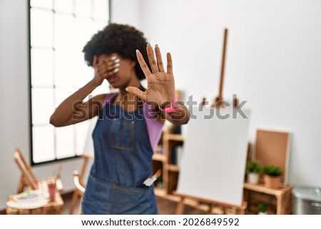 Young african american woman with afro hair at art studio covering eyes with hands and doing stop gesture with sad and fear expression. embarrassed and negative concept. 