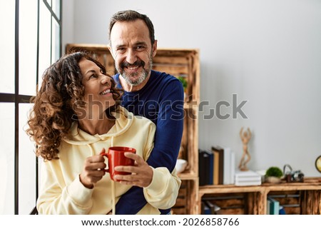 Middle age hispanic couple smiling happy and drinking coffee. Leaning on the window at home. Royalty-Free Stock Photo #2026858766