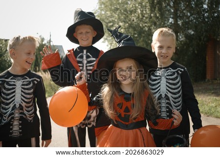 Halloween kids. Jack-o-lantern. Children in carnival costumes outdoors. Witch and skeletons. Friends are having fun with orange black balloons. Slow motion. Brothers and sister celebrate halloween