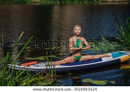 girl, blonde in a green swimsuit on a sup board on the lake doing yoga