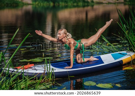 girl, blonde in a green swimsuit on a sup board on the lake doing yoga