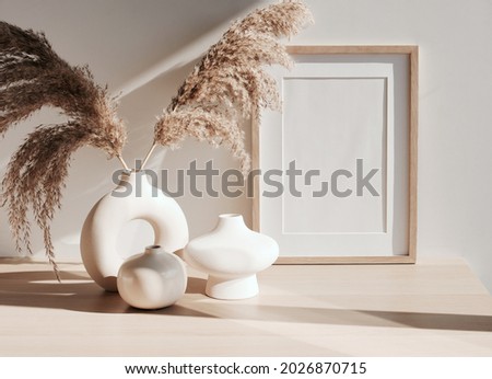 frame mockup on beige table, modern beige ceramic vases with dry grass and sunlight shadow.Neutral color. White wall background. Scandinavian interior. Copy space.