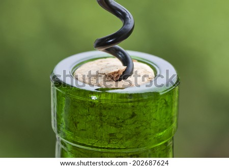 Opening a wine bottle with a corkscrew on green background