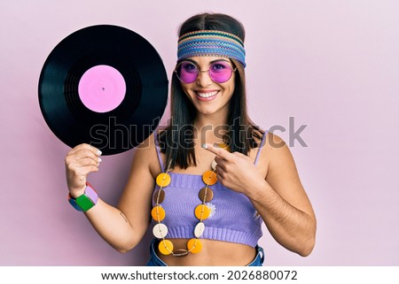 Young brunette woman wearing hippie style holding vinyl disc smiling happy pointing with hand and finger 