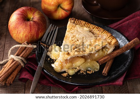 Slice of apple pie on a plate with apples and cinnamon sticks in background Royalty-Free Stock Photo #2026891730