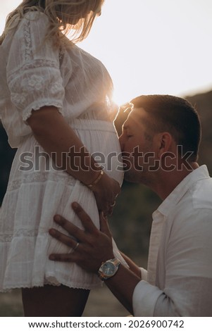 Handsome happy man kissing wife's pregnant belly at sunrise closeup